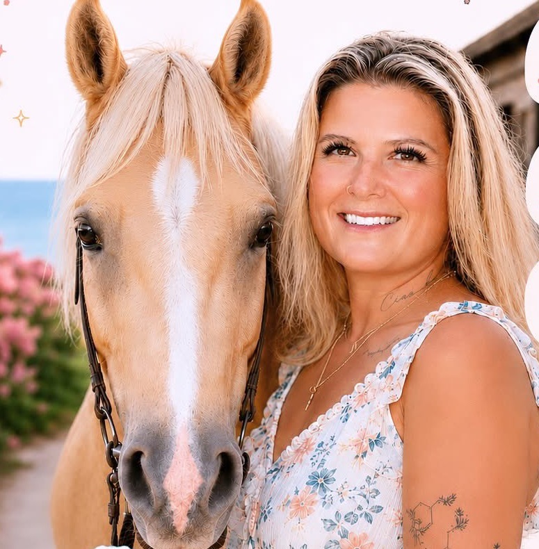 Alexandra Abergel smiling beside a palomino horse near the coast